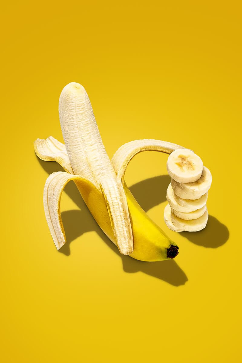 A partially peeled banana, with extra banana slices on the side