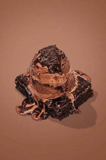 A chocolate brownie topped with a scoop of chocolate ice cream