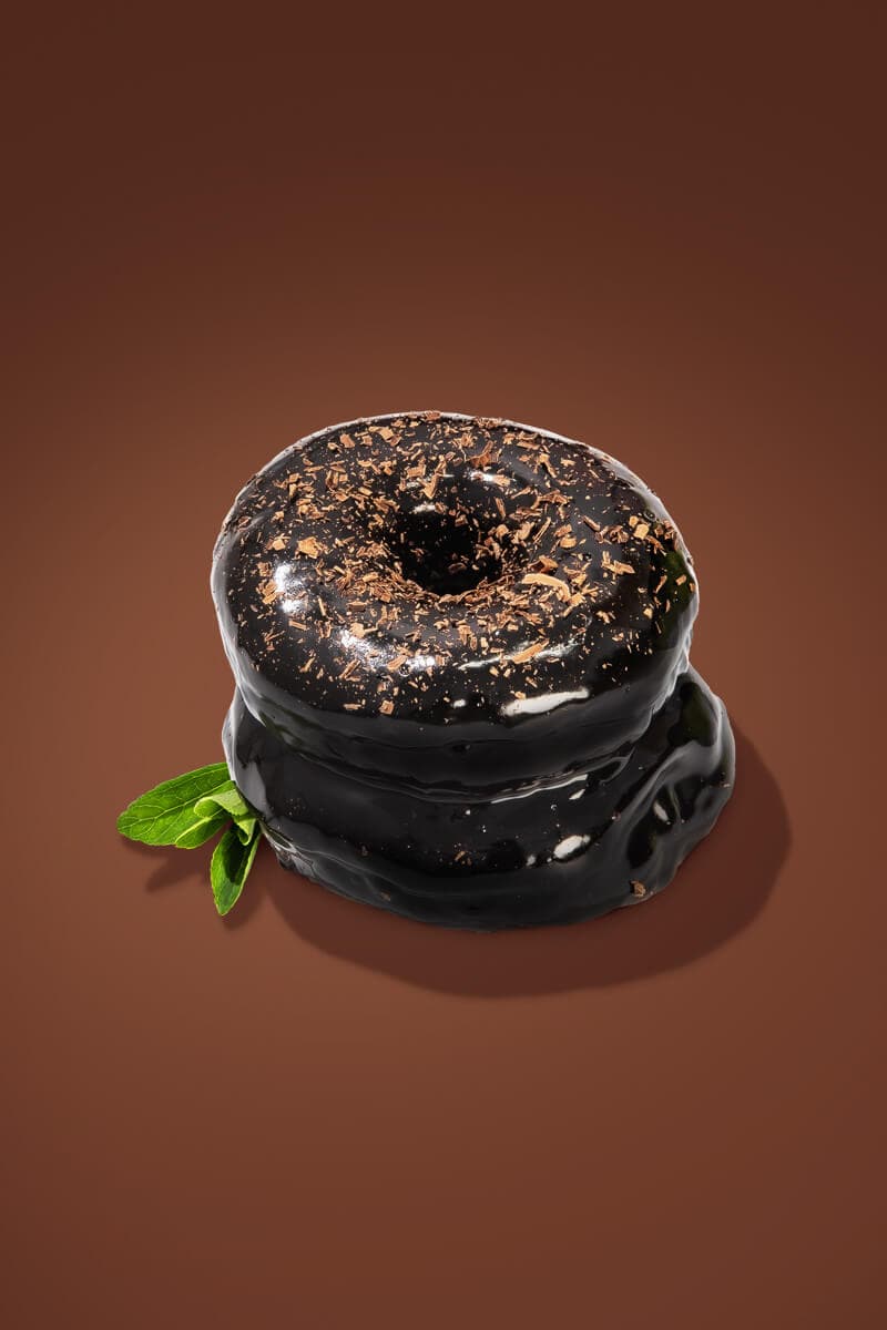 Two chocolate glazed donuts with extra chocolate shavings on top