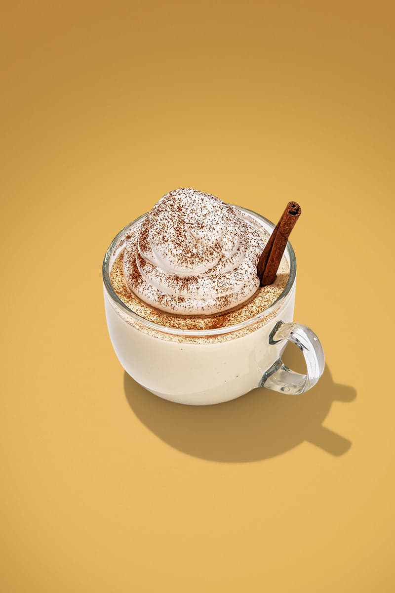 A glass of eggnog, garnished with whipped cream and cinnamon