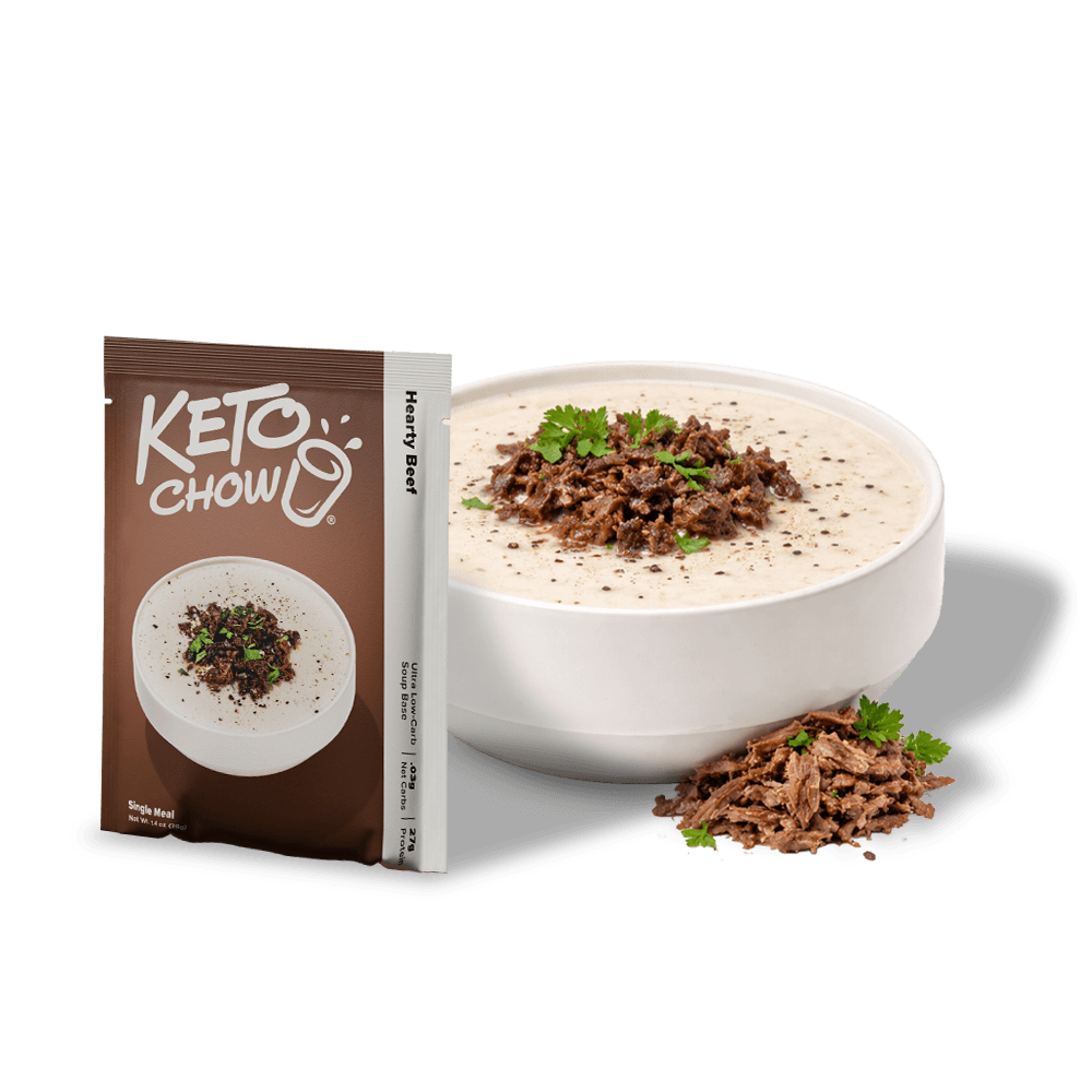 KETO CHOW Hearty Beef Soup Base brown single-serve packet showing logo, Hearty Beef, .03g Net Carbs, 27g Protein. Next to it, a white bowl of creamy soup topped with beef crumbles and parsley.