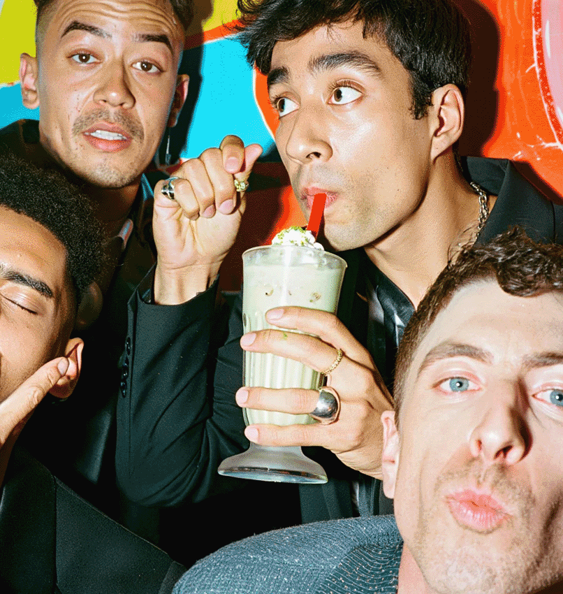 A woman with tan skin and long, dark brown hair is smiling and looking directly at the camera. She is holding a creamy, pistachio green shake.