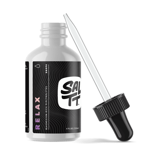 SALTT Relax magnesium-rich electrolyte drops in a sleek white bottle with a black label featuring a subtle wavy pattern, a bold white SALTT logo, and vibrant purple vertical Relax text. A separate black dropper with a silver pipette is shown beside it.